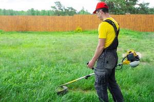 un' maschio giardiniere falcia il verde erba di il prato nel il Giardino dietro la casa con un' benzina tosaerba. trimmer per il cura di un' giardino tracciare foto