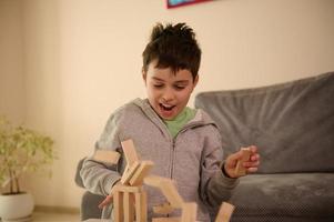 avvicinamento di un' bello scuola anziano europeo ragazzo giocando tavola Giochi e sembra sorpreso quando il suo costruito struttura a partire dal di legno blocchi caduta fuori uso. formazione scolastica tempo libero e tavola Giochi concetto foto