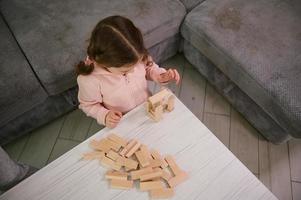 superiore Visualizza di un' creativo prescolastico bambino, concentrato bambino ragazza su edificio con di legno blocchi mattoni. educativo tavola gioco e evolutivo inteligente passatempo. bene il motore abilità sviluppo concetto foto