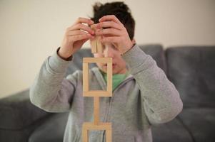 avvicinamento. caucasico bello perplesso scuola ragazzi mani, concentrato su costruzione di complesso alto struttura a partire dal di legno blocchi. bene il motore abilità, concentrazione e educativo tempo libero concetto foto