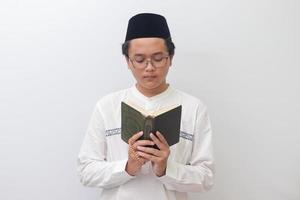 ritratto di giovane asiatico musulmano uomo lettura e recitando santo libro di Corano sul serio. isolato Immagine su bianca sfondo foto