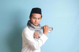 ritratto di asiatico musulmano uomo nel bianca koko camicia fare marziale arti gesto o pencak silat. isolato Immagine su blu sfondo foto