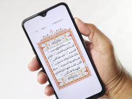 Indonesia, aprile 2023. mano Tenere mobile Telefono mostrando Corano App nel esso foto