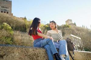 allegro asiatico donne seduta su pietra confine e sorridente foto