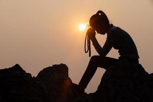 silhouette di donna raccolta il suo mani nel culto, donna preghiere per Dio, cristiano religione concetto sfondo. foto