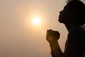 silhouette di donna raccolta il suo mani nel culto, donna preghiere per Dio, cristiano religione concetto sfondo. foto