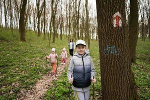 famiglia escursioni a piedi insieme. ragazzo vicino pista marcatore su albero a primavera foresta. foto