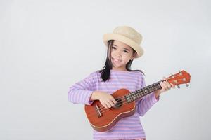 carino poco ragazza nel costume da bagno giocando ukulele. contento vacanza concetto. foto