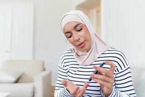 Arabo donna utilizzando lancetta su dito per controllo sangue zucchero livello di glucosio metro, assistenza sanitaria e medico, diabete, glicemia concetto foto