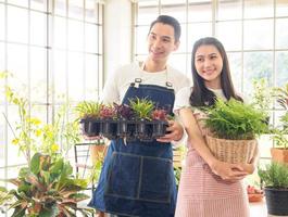 giardiniere giovane asiatico uomo donna famiglia Due persona In piedi sorridente guardare mano Tenere Aiuto decorare il tavolo albero foglia verde nel calma opera negozio casa pianta finestra parete. passatempo lavoro contento e cura concetto foto