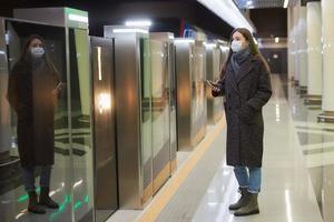 una donna con una maschera medica sta aspettando un treno in arrivo sulla metropolitana foto