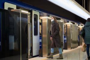 una ragazza con una mascherina chirurgica mantiene le distanze sociali in una stazione della metropolitana foto