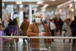 un uomo con una maschera facciale tiene in mano una tazza di caffè nel centro commerciale foto