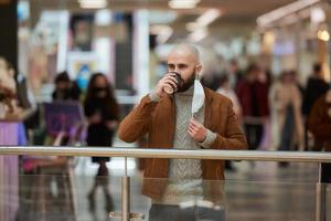 un uomo tiene in mano una maschera mentre beve il caffè nel centro commerciale foto
