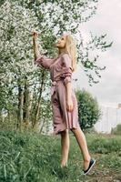 bionda ragazza su un' primavera camminare nel il giardino con ciliegia fiori. femmina ritratto, avvicinamento. un' ragazza nel un' rosa polka punto vestire. foto