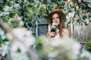 bellissimo giovane ragazza nel bianca vestito e cappello nel fioritura Mela frutteto. fioritura Mela alberi con bianca fiori. foto