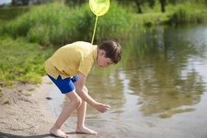 il ragazzo è attraente pesce con un' farfalla netto su il lago. foto