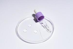 siero cosmetico per pipette su una capsula di Petri su sfondo bianco. concetto di cosmetologia e prodotti farmaceutici. peeling acido, olio per il viso, collagene. foto