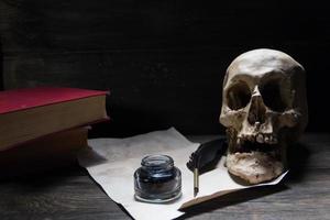 libri, umano cranio, penna e carta su rustico legna foto