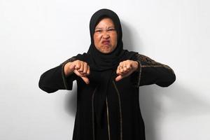 irritato mezzo anziano asiatico donne indossare hijab mostrare pollici giù gesto, dare negativo opinione, giudicare cattivo foto