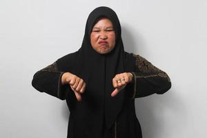 irritato mezzo anziano asiatico donne indossare hijab mostrare pollici giù gesto, dare negativo opinione, giudicare cattivo foto