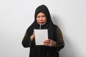 mezzo anziano asiatico donne indossare hijab pensiero qualcosa sul serio mentre Tenere un' penna e libro isolato su bianca sfondo. foto
