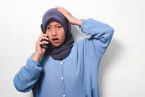 giovane asiatico ragazza nel hijab sembra scioccato mentre utilizzando mobile Telefono foto