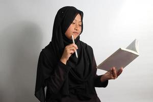 riflessivo giovane asiatico ragazza alunno interessato nel pensiero mentre Tenere un' libro e penna isolato su bianca sfondo foto