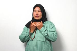 mezzo anziano asiatico donne indossare hijab prega per Dio e Tenere preghiera perline isolato al di sopra di bianca sfondo. foto