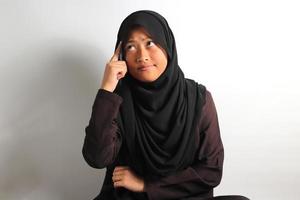 giovane asiatico ragazza alunno nel nero hijab pensiero di domanda isolato su bianca sfondo. foto