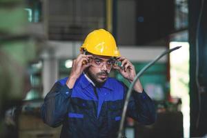 esperto ingegneri o lavoratori Tenere un' bianca cappello contento per opera nel un industriale fabbrica. foto