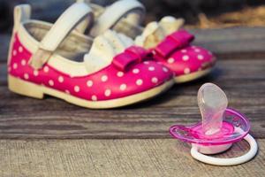 bambino scarpe e un' pacificatore su di legno sfondo. foto