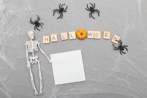 iscrizione Halloween, ragno ragnatela e ragni su grigio sfondo con scheletro e carta etichetta foto