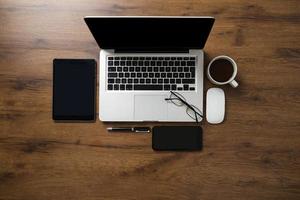 area di lavoro con laptop, smartphone, tablet, tazza di caffè, occhiali e penna foto
