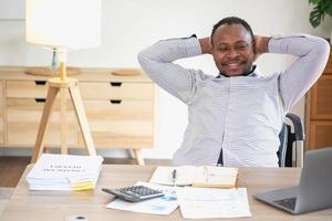 africano americano uomo d'affari sorridente rilassato e attraversato braccia dopo analisi e ricerca a casa ufficio foto