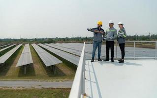 su il tetto di un' grande solare energia Conservazione stazione edificio un' squadra di elettrico energia ingegneri ispezionando solare pannelli quello avere stato installato su centinaia di acri di campi. foto