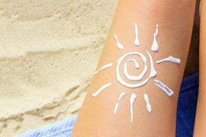 donna prendere il sole su il spiaggia con un' disegno di sole su sua gamba con protezione solare crema foto
