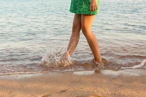 gamba di donna in esecuzione su spiaggia con acqua schizzi. estate vacanza. gambe di un' ragazza a piedi nel acqua su tramonto foto