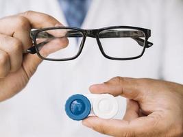 medico maschio che mostra un paio di occhiali neri e lenti a contatto