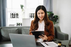 asiatico avvocato donna Lavorando con un' il computer portatile e tavoletta nel legge ufficio. legale e legale servizio concetto. guardare a telecamera foto