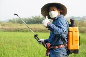 asiatico contadino è spruzzatura biologico fertilizzante a risaia campo. pollice su. concetto utilizzando amichevole Prodotto con ambiente agricoltura con no sostanze chimiche usando. sicurezza con utente e ambiente. foto