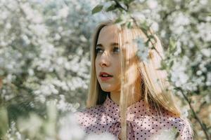 bionda ragazza su un' primavera camminare nel il giardino con ciliegia fiori. femmina ritratto, avvicinamento. un' ragazza nel un' rosa polka punto vestire. foto