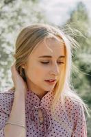 bionda ragazza su un' primavera camminare nel il giardino con ciliegia fiori. femmina ritratto, avvicinamento. un' ragazza nel un' rosa polka punto vestire. foto