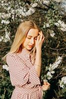 bionda ragazza su un' primavera camminare nel il giardino con ciliegia fiori. femmina ritratto, avvicinamento. un' ragazza nel un' rosa polka punto vestire. foto