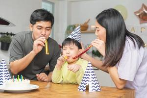 contento compleanno festa nel famiglia, asiatico giovane genitore padre, madre e poco carino ragazzo o bambino festeggiare, soffiaggio candele su il torta e decorato palloncini, celebrazione a casa. bello momenti foto