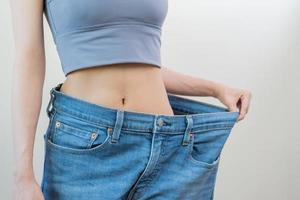 forma snello, magro vita, attraente sottile asiatico giovane donna, mano mostrare forma sua peso perdita, indossare nel grande, grande o oversize jeans, eccesso perdere di dieta e esercizio. persone corpo in forma sano. foto