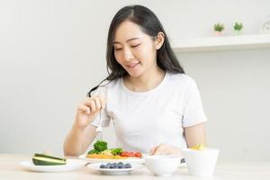 dieta, dieta asiatico giovane donna, ragazza mangiare, Tenere forchetta a broccoli, dieta Piano nutrizione con fresco verdure insalata, godere pasto su tavolo a casa. dietologo di sano, nutrizione di peso perdita. foto