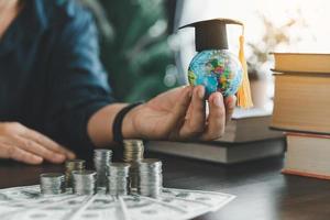 mano Tenere la laurea berretto su globo con pila moneta. concetto di Salvataggio i soldi per un' Borsa di studio per studia all'estero a un' Università livello. finanziario pianificazione contabilità idee per futuro formazione scolastica. foto