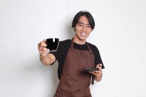 ritratto di attraente asiatico barista uomo nel Marrone grembiule servendo un' tazza di caffè per il cliente. isolato Immagine su bianca sfondo foto