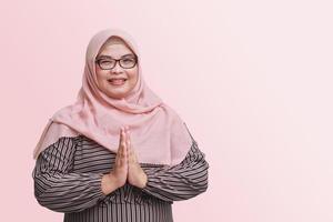 ritratto di allegro asiatico donna con hijab, mostrando scusarsi e benvenuto mano gesto. pubblicità concetto. isolato Immagine su rosa sfondo foto